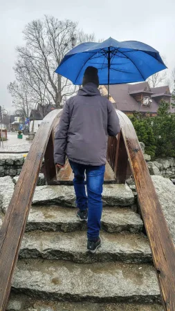Muž s modrým deštníkem kráčí po kamenných schodech mostu v dešti