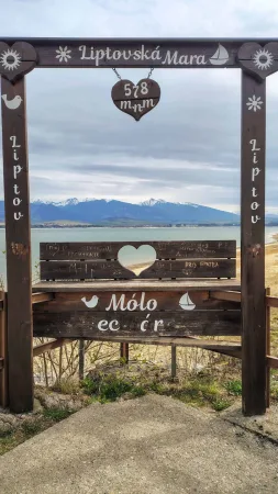 Dřevěná vyhlídková brána s nápisem Liptovská Mara a výhledem na jezero a hory.