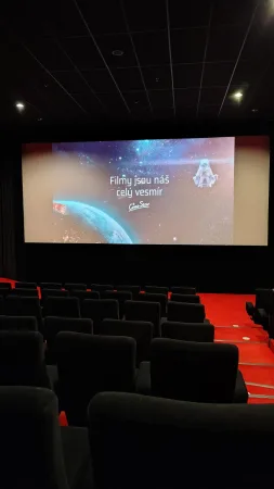 Prázdný kinosál s červenými sedačkami a promítaným reklamním sloganem na plátně.