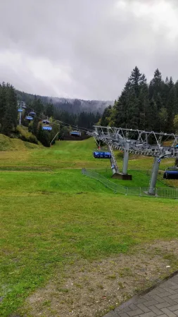 Sedačková lanovka vede přes zelenou louku k zamlženým horám na podzim.