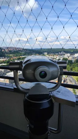 Mincový vyhlídkový dalekohled na střeše s panoramatem města v pozadí.