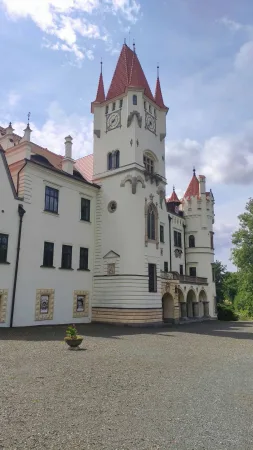 Bílá fasáda zámku Žinkovy zdobená erby pod věží s cimbuřím a hodinami