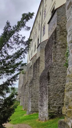 Kamenné opevnění zámku Orlík nad Vltavou lemované vzrostlým stromem s výhledem na vodní nádrž