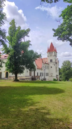 Zámek Žinkovy s červenými střechami vyhlížející z anglického parku za slunečného dne