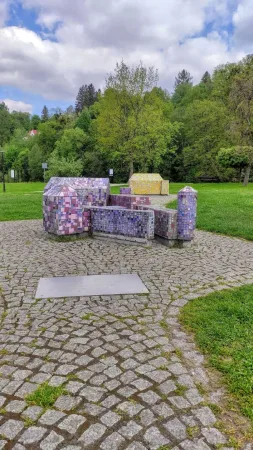 Fialová mozaiková miniatura hradního komplexu obklopená zelení Parku miniatur ve Wisle