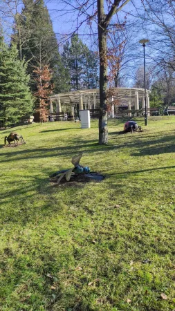 Travnatá plocha se sochami hmyzu a dřevěným altánem v pozadí zoo
